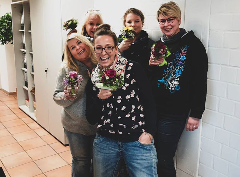 2509_InternationalWomensDay_KK 5 ladies from Kaiser and Kühne smiling, holding a flower, looking at the camera, and celebrating International Women's Day.