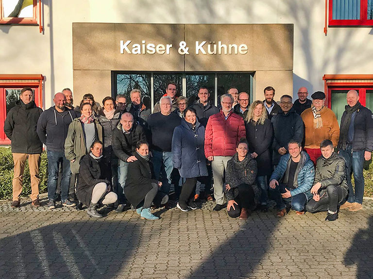 Angestellte von Kaiser und Kühne stehen lächelnd vor dem Firmengebäude
