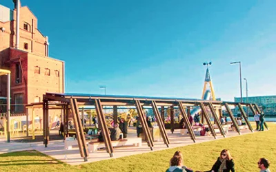 Three adults are sitting in a meadow, and next to them is the play structure from the ‘Harte Mill’ project